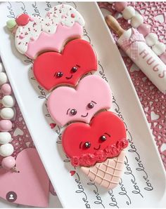 three heart shaped cookies sitting on top of a white platter next to candy sticks