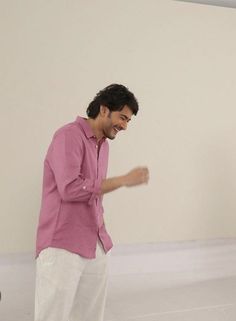 a man in pink shirt and white pants standing next to a painting on the wall