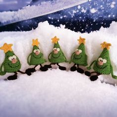 five green crocheted christmas trees with gold stars on their heads are lined up in the snow