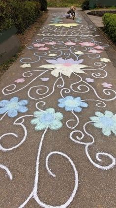 the sidewalk is decorated with chalk and has flowers on it, while a dog stands in the distance