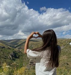 a woman making a heart shape with her hands in the air while standing on top of a hill