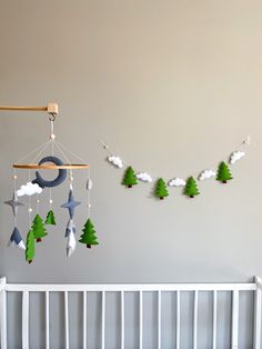 a baby crib with a mobile hanging from it's side and trees on the wall