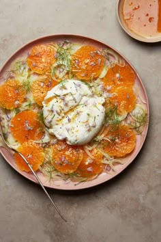 a pink plate topped with orange slices and whipped cream next to a bowl of sauce