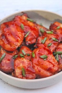 a white bowl filled with meat covered in sauce and garnished with green onions