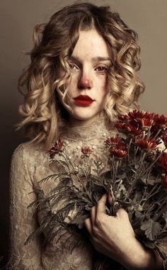 a woman with red lipstick holding flowers in her hands