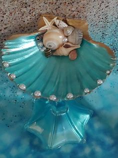 there is a blue glass shell with shells on it and pearls in the bottom half