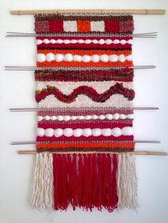 a wall hanging made up of different colored yarns and wooden sticks with white balls on them