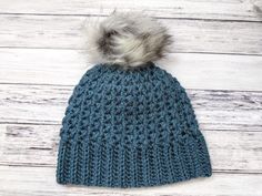 a blue knitted hat with a grey pom - pom sitting on top of it