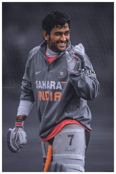 a man in grey and orange jersey holding a baseball glove on his left hand while smiling at the camera