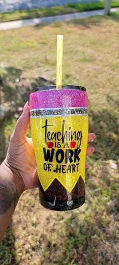 a person holding up a yellow and pink cup with straw in it that says teaching is work of heart