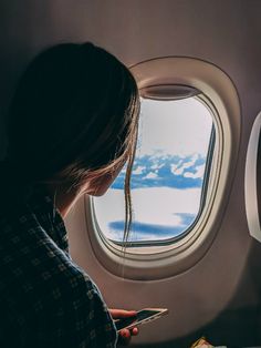 a woman is looking at her cell phone while sitting on an airplane window sill