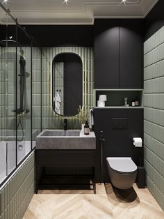 a modern bathroom with green tiles on the walls and wood flooring, along with a white toilet