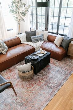 a living room with brown leather couches and pillows on top of a large rug