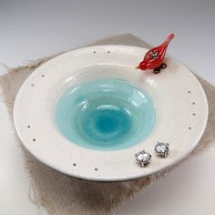 a small red bird sitting on top of a white bowl filled with blue liquid and silver studs