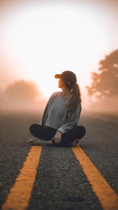 a woman sitting in the middle of an empty road with her skateboard on it