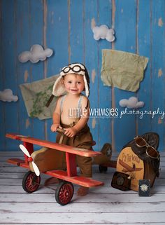 a little boy sitting on top of a wooden plane next to an old fashioned suitcase