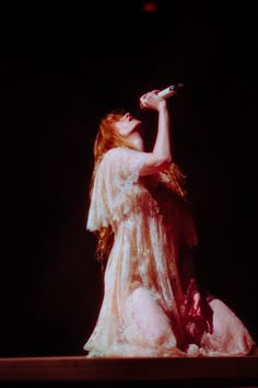 a woman in a white dress holding a microphone on top of a wooden table with her legs crossed