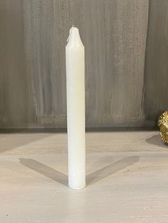 a white candle sitting on top of a wooden table next to a gold leafy object