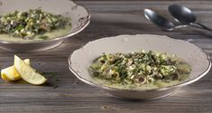 two white bowls filled with soup next to lemon wedges and spoons on a wooden table