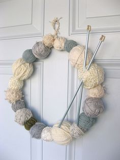 a yarn wreath with knitting needles hanging from the front door, decorated with balls of yarn