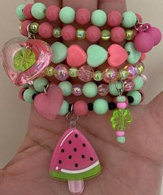 a hand holding several bracelets with various charms on each one arm and a watermelon charm hanging from the middle