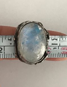 "This unusual ring has a large oval shaped cabochon moonstone that is bezel set in south-west fashion. The band looks almost like branchlike wavy lines. The silver setting which is raised to hug the stone has a hammered and pinched look and has some areas where it looks like the silver has split which is part of the design. The face of this ring is 3/4\" long and about 1\" at its widest. It shows as a size 4 1/4 on my ring sizer, but fits my size 5 finger. Please see all photos for details, as w Bohemian Oval Cabochon Moonstone Ring, Unique Adjustable Oval Moonstone Ring, Artisan Oval Moonstone Ring, Bohemian Untreated Oval Moonstone Ring, Bohemian Oval Untreated Moonstone Ring, Handcrafted Oval Moonstone Ring, Unique Cabochon Moonstone Ring, Handmade Artisan Oval Moonstone Ring, Adjustable Oval Untreated Moonstone Ring