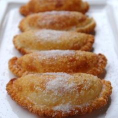 four pastries are lined up on a white plate with powdered sugar toppings