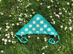 a crocheted hat laying in the grass with daisies around it