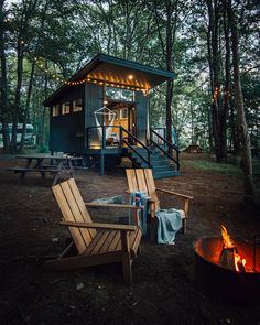 there is a small cabin in the woods with two chairs and a fire pit next to it