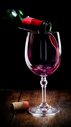 a glass filled with red wine next to a corkscrew on top of a wooden table