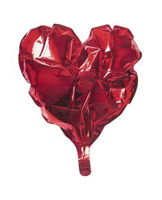 a red heart shaped object is hanging on a white wall and it appears to be wrapped in foil