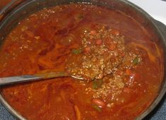 a large pot filled with meat and vegetables on top of a stove next to a wooden spoon