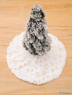 a small christmas tree sitting on top of a white cloth covered placemat with snow flakes