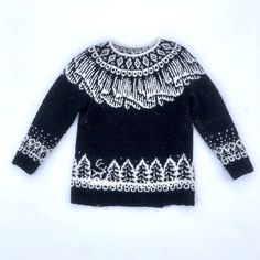 a black and white sweater with an intricate design on the front, sitting on a white surface