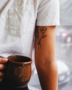 a person with a flower tattoo on their arm holding a coffee mug in front of a window