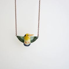 a small bird is hanging from a chain on a white wall and it's yellow, green, and blue color scheme