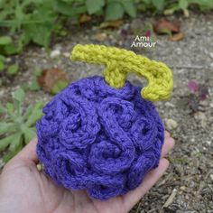 a hand holding a crocheted purple ball with a yellow loop on it's end