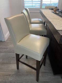 a set of four white leather chairs sitting in front of a counter with a window