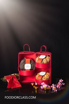 two red boxes filled with pastries on top of a black table next to flowers