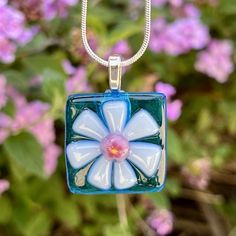 a glass pendant with a flower on it in front of purple and white flowers,