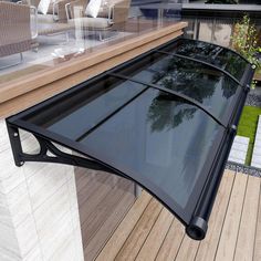 a black awning over a wooden deck next to a glass wall and patio furniture