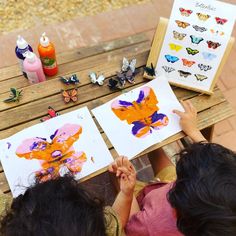 two children are sitting at a picnic table and painting pictures with butterflies on the paper