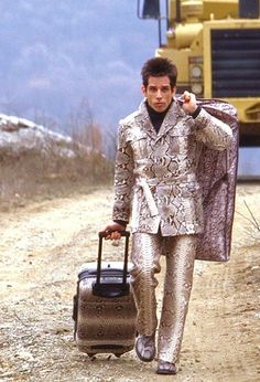 a man walking down a dirt road with a suit case and suitcase in his hand