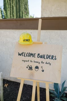 a sign with a hard hat on top of it in front of a building that says welcome builder