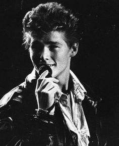 black and white photograph of a young man holding a microphone in his right hand while wearing a leather jacket