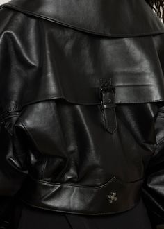 This oversized black leather jacket features a bold, structured design with voluminous sleeves and a wide collar. The jacket is accented by a diagonal front zipper and a wide belt that cinches the waist, blending avant-garde style with a sleek, modern edge. DETAILS: - Belted waist - Buckle embellishment on back - Option for stand collar COLOR: Black SIZE & FIT: Model is 32 bust, 25 waist, 38 hip and wearing a size S. CARE INSTRUCTIONS: Dry clean recommended. Air dry. Do not machine dry. Black Leather Outerwear With Belt, Designer Black Outerwear With Belted Cuffs, Black Designer Outerwear With Belted Cuffs, Luxury Black Outerwear With Belt Loops, Luxury Black Belted Outerwear, Black Leather Outerwear With Belted Cuffs, Chic Black Biker Jacket With Belt Loops, Luxury Belted Biker Jacket For Fall, Luxury Black Leather Jacket With Belt Loops