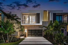 a modern home at night with palm trees in the foreground and driveway leading up to it