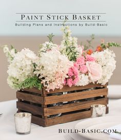 a wooden crate filled with flowers sitting on top of a white table covered in pink and white flowers