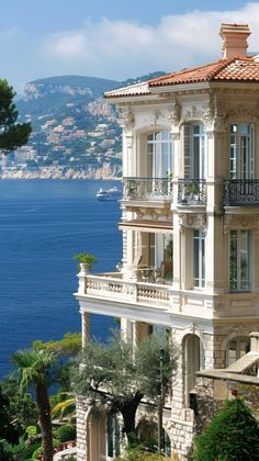 an ornate building with balconies overlooks the blue water and hills behind it