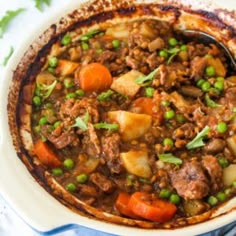 a pot filled with meat and vegetables on top of a white cloth next to a spoon